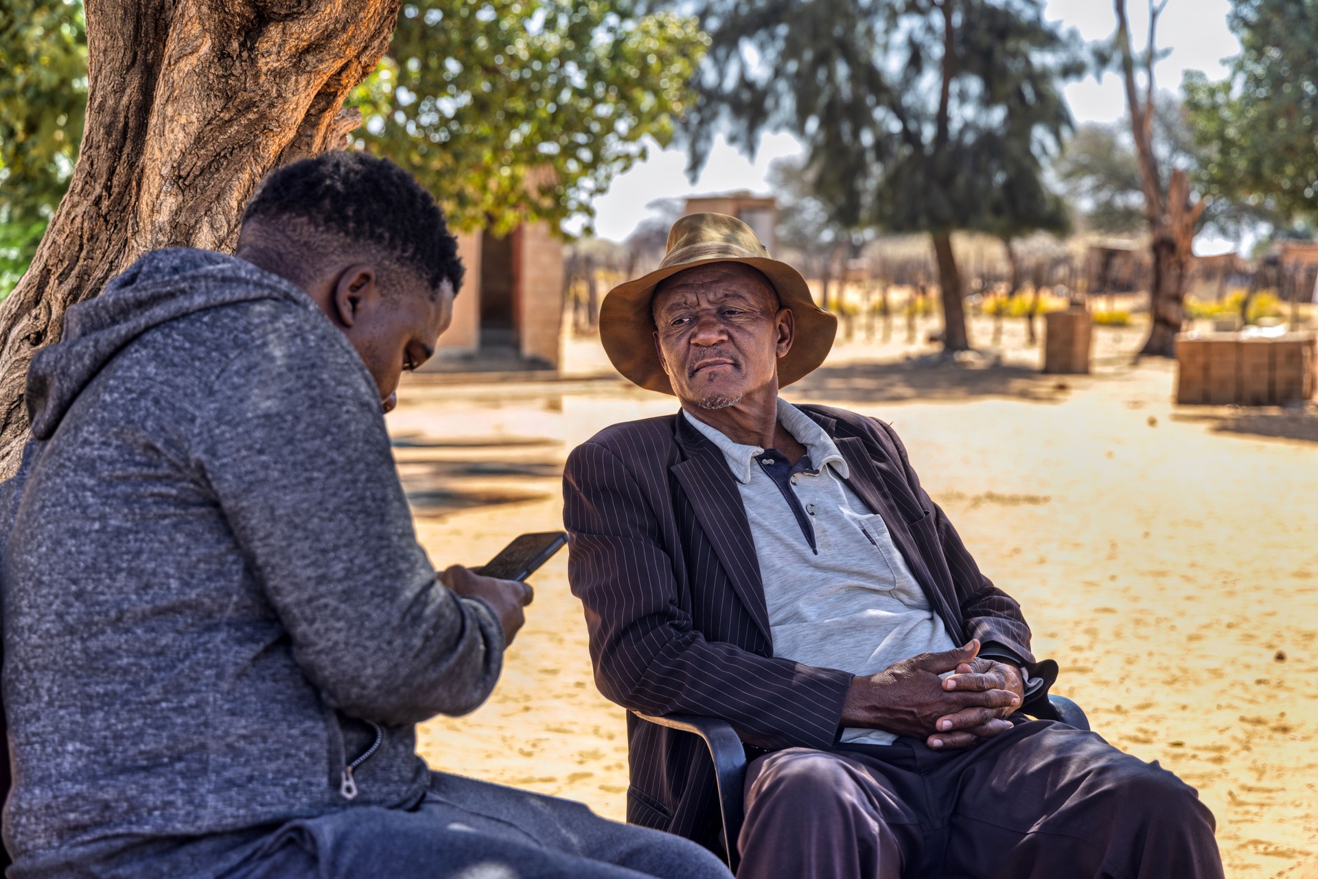 African village, portrait social worker volunteer charity worker using smartphone, Africa old man in front of the house, using technology to improve life in rural areas,